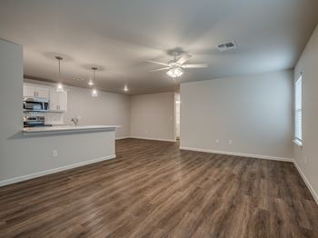 an empty living room with a kitchen in the background